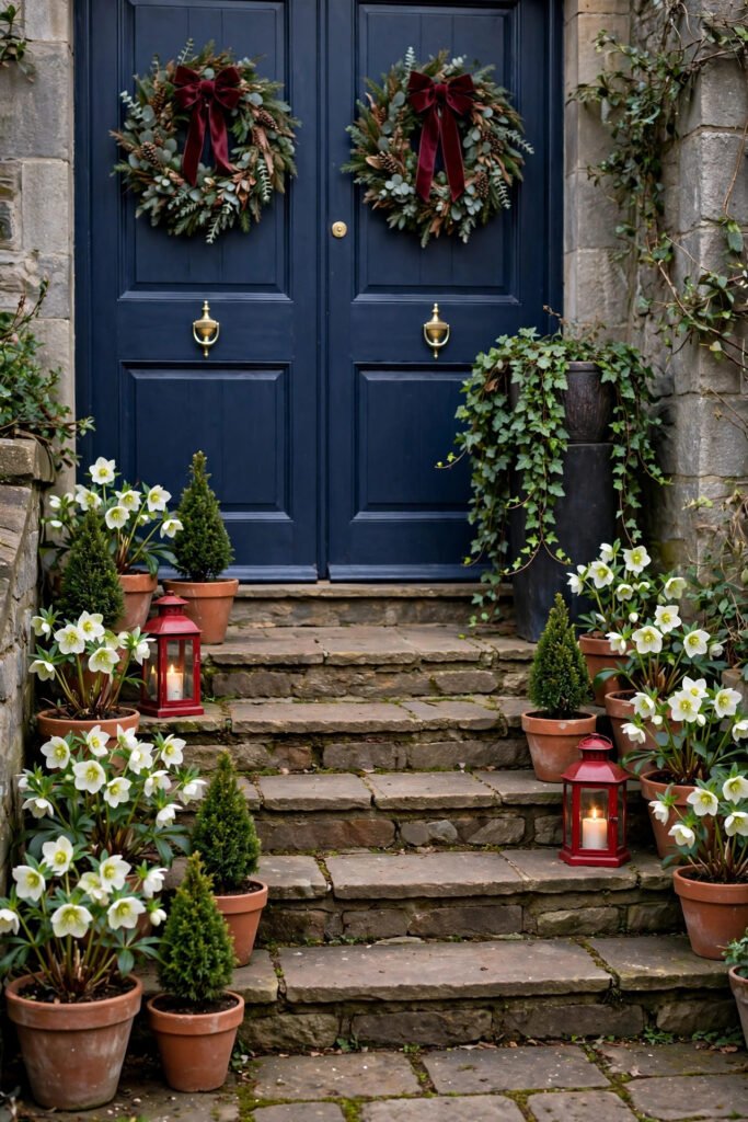 Stone steps lined with terracotta pots of white hellebores and small cone-shaped evergreens, tall dark planter spilling ivy, red lanterns with candles, two navy doors with wreaths and burgundy velvet bows